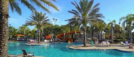 A swimming pool area with palm trees, lounge chairs, and a small waterfall feature.