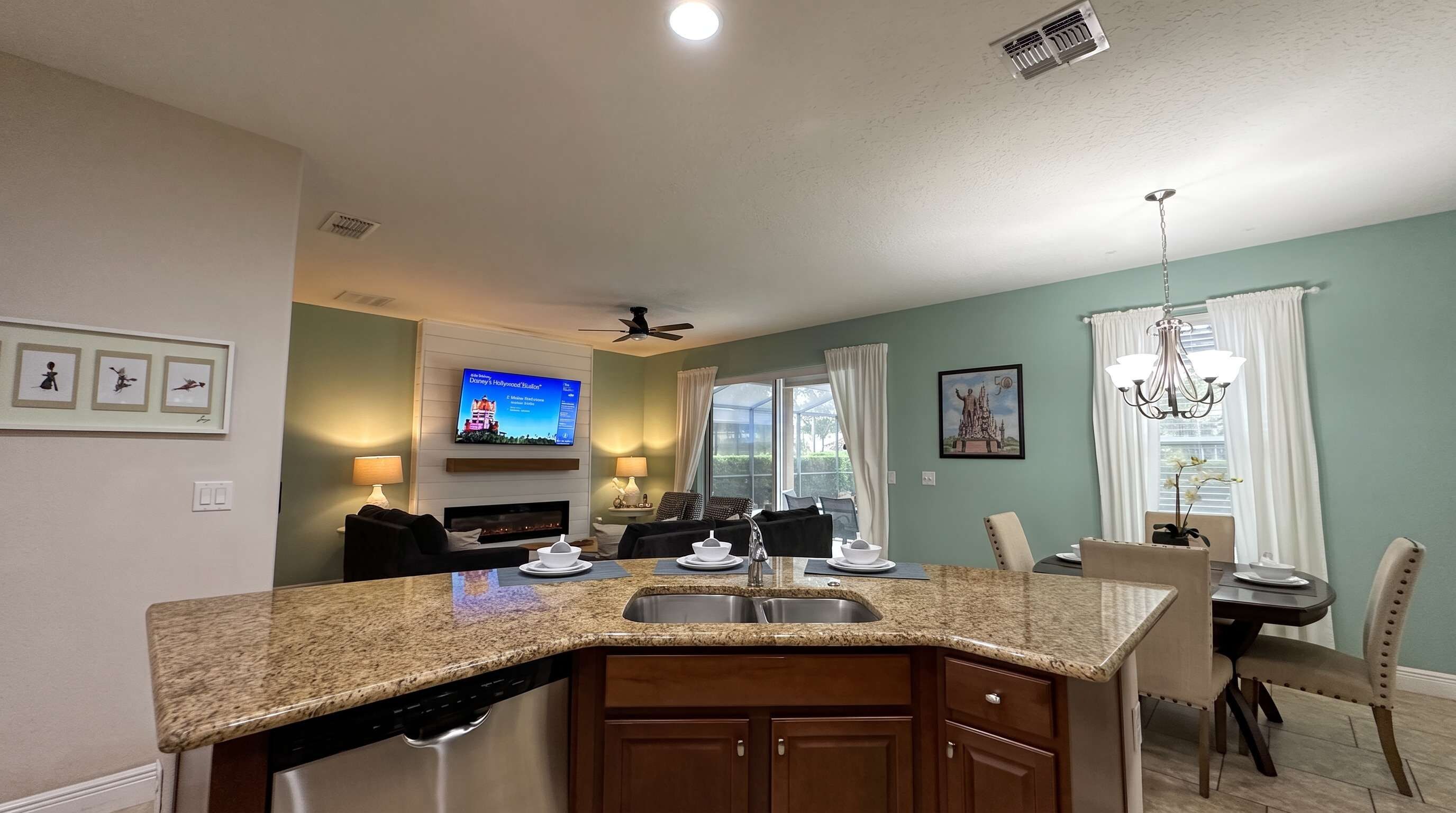 A modern kitchen with granite countertops, a built-in dishwasher, and a dining area with a chandelier.