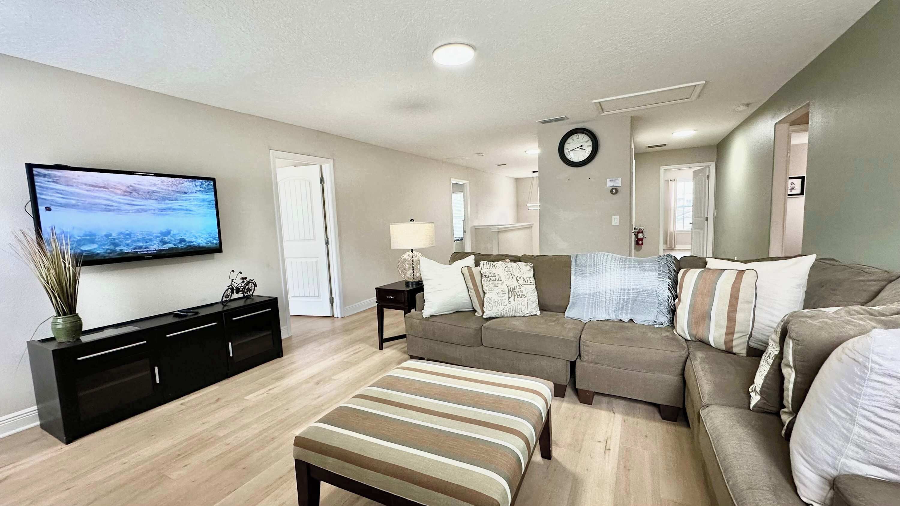 A modern living room with a flat-screen TV, a sofa set, a coffee table, and a dining area with a black console and a vase.