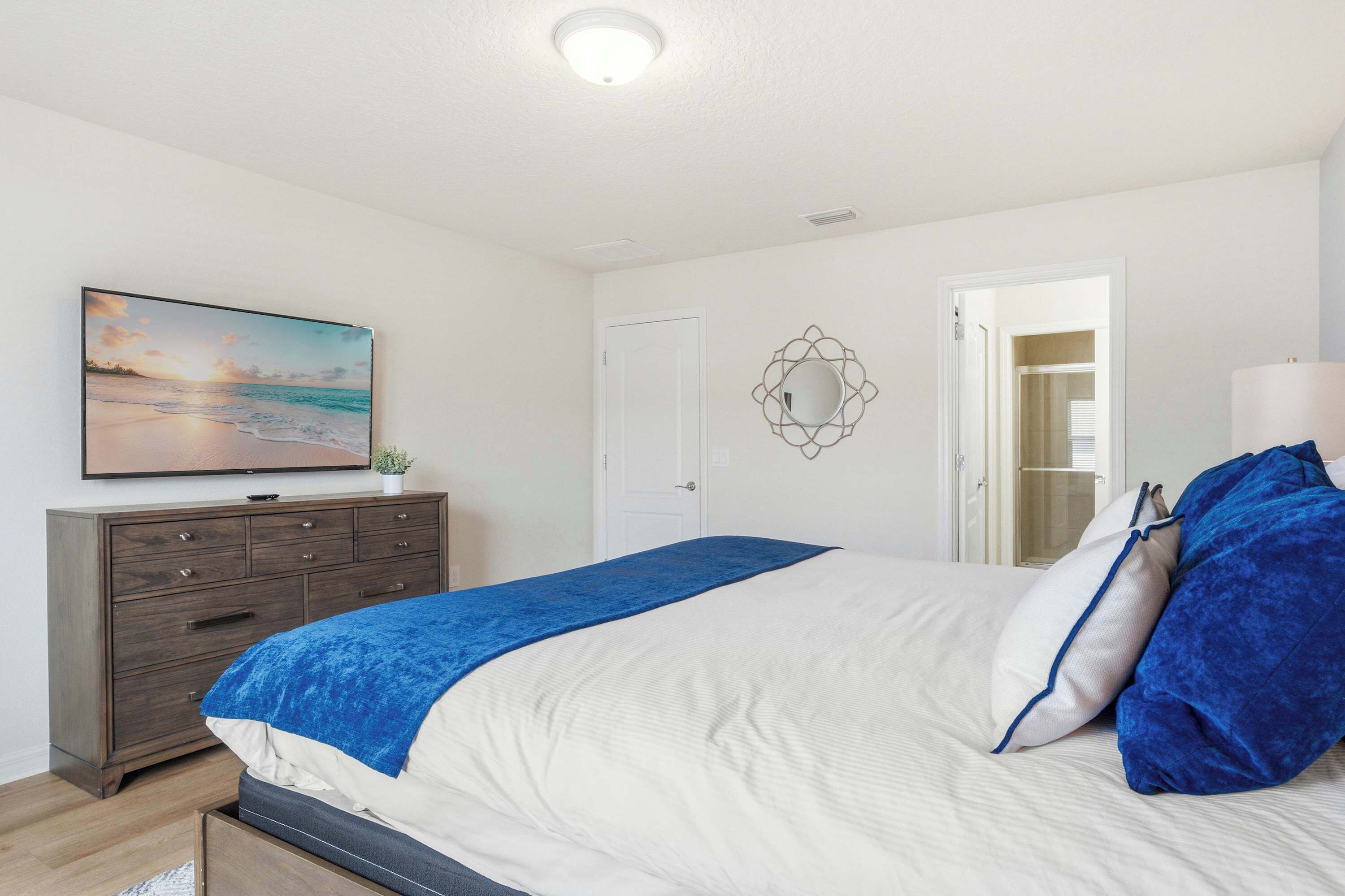 A bedroom with a bed, a dresser, a painting, a mirror, and a door.