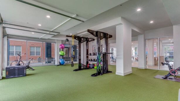 Un gimnasio amplio e interior con piso verde, equipo de ejercicio y ventanas grandes que ofrecen vistas al exterior.