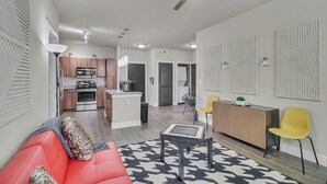 Un salon moderne avec un canapé rouge, une table basse et un coin repas avec des chaises jaunes.