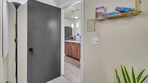 Un couloir avec une porte gris foncé, un lampadaire blanc et une étagère murale contenant des livres de voyage.