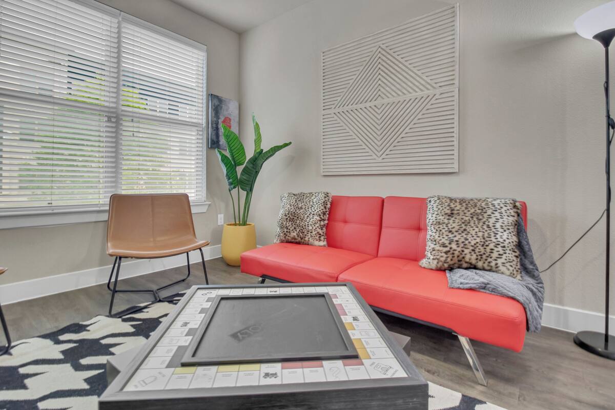Ein Wohnzimmer mit einem roten Sofa, einem Sessel, einem Couchtisch, einer Topfpflanze und einem Wandbild.