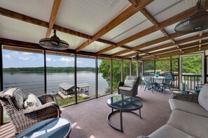 A covered outdoor area with wicker furniture, a round table, and a view of a lake. - Lakefront Sunsets| Private Dock | Kayaks & Fishing (Hodges)