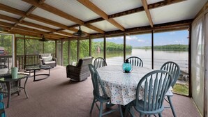 Ein überdachter Außenbereich mit Tisch und Stühlen, einem Ventilator und Blick auf einen See.