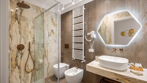 Une salle de bain moderne avec une douche à parois de verre, des toilettes blanches, un bidet, un meuble-lavabo doté d’un grand miroir et un porte-serviettes.