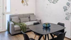 Un espace repas moderne avec une table et des chaises noires, un canapé gris et une fresque murale.