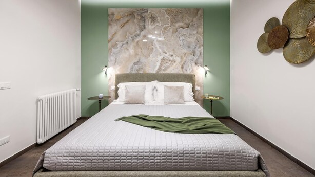 Une chambre moderne avec un grand lit, une tête de lit en marbre et un mur d’accent vert.