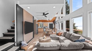Una sala de estar moderna con un amplio sofá modular, un televisor de pantalla plana montado en la pared y una escalera que lleva a un nivel superior.