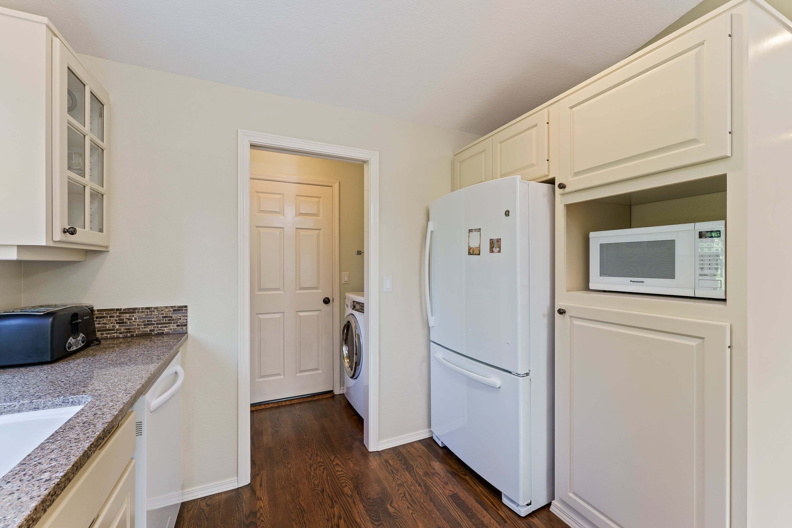 A compact kitchen with white cabinets, a built-in microwave, a refrigerator, a washing machine, and a toaster.