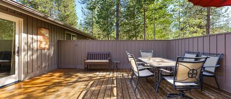 A wooden deck with a table and chairs, a bench, and a red umbrella.