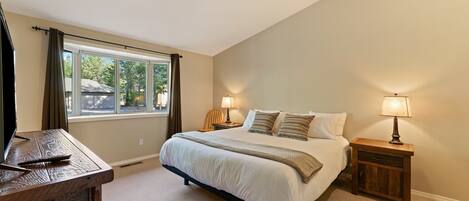 A bedroom with a large bed, two bedside tables with lamps, a wooden desk, and a window with curtains.