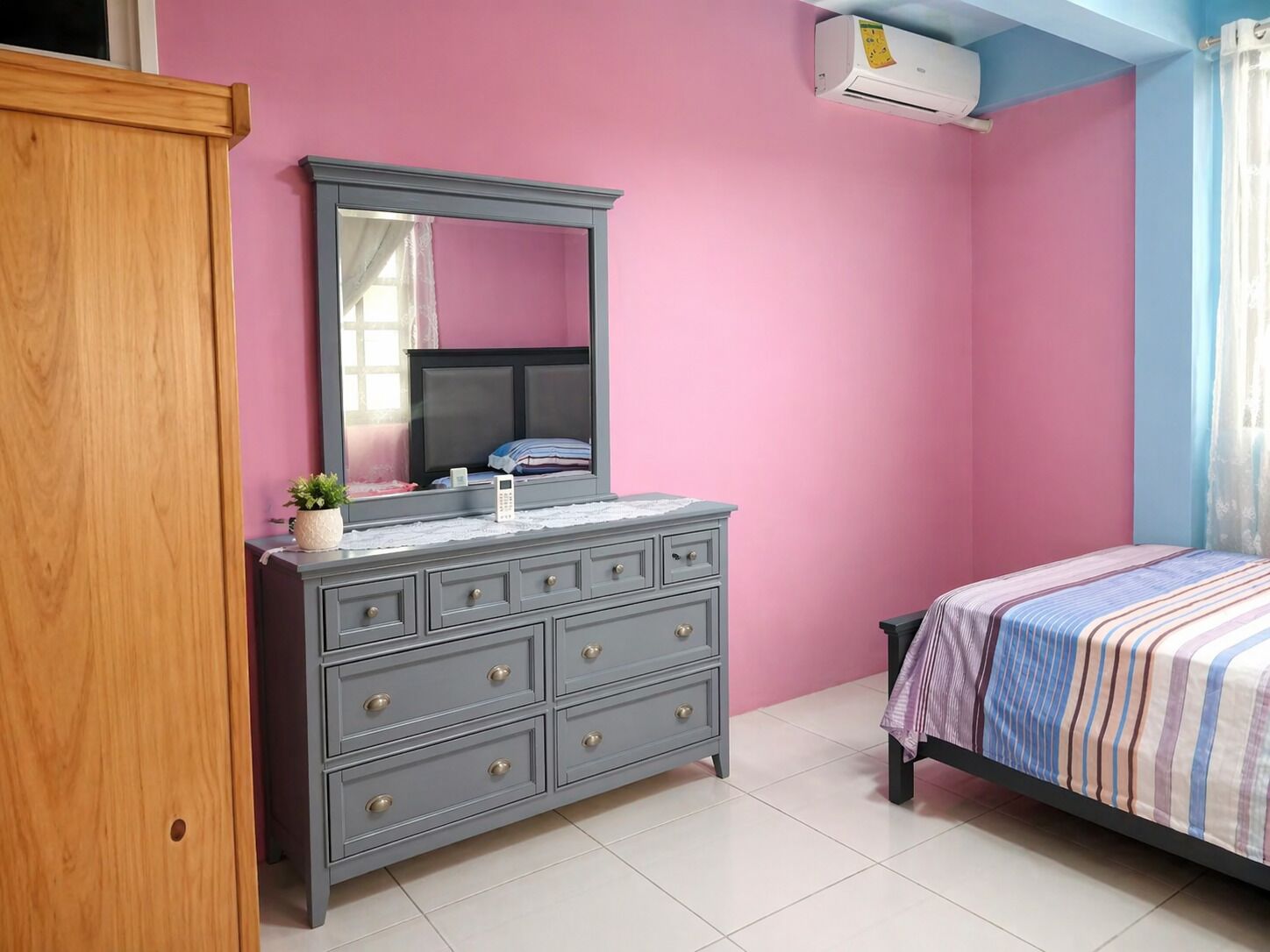 A bedroom with a dresser, a bed, and a window with curtains.