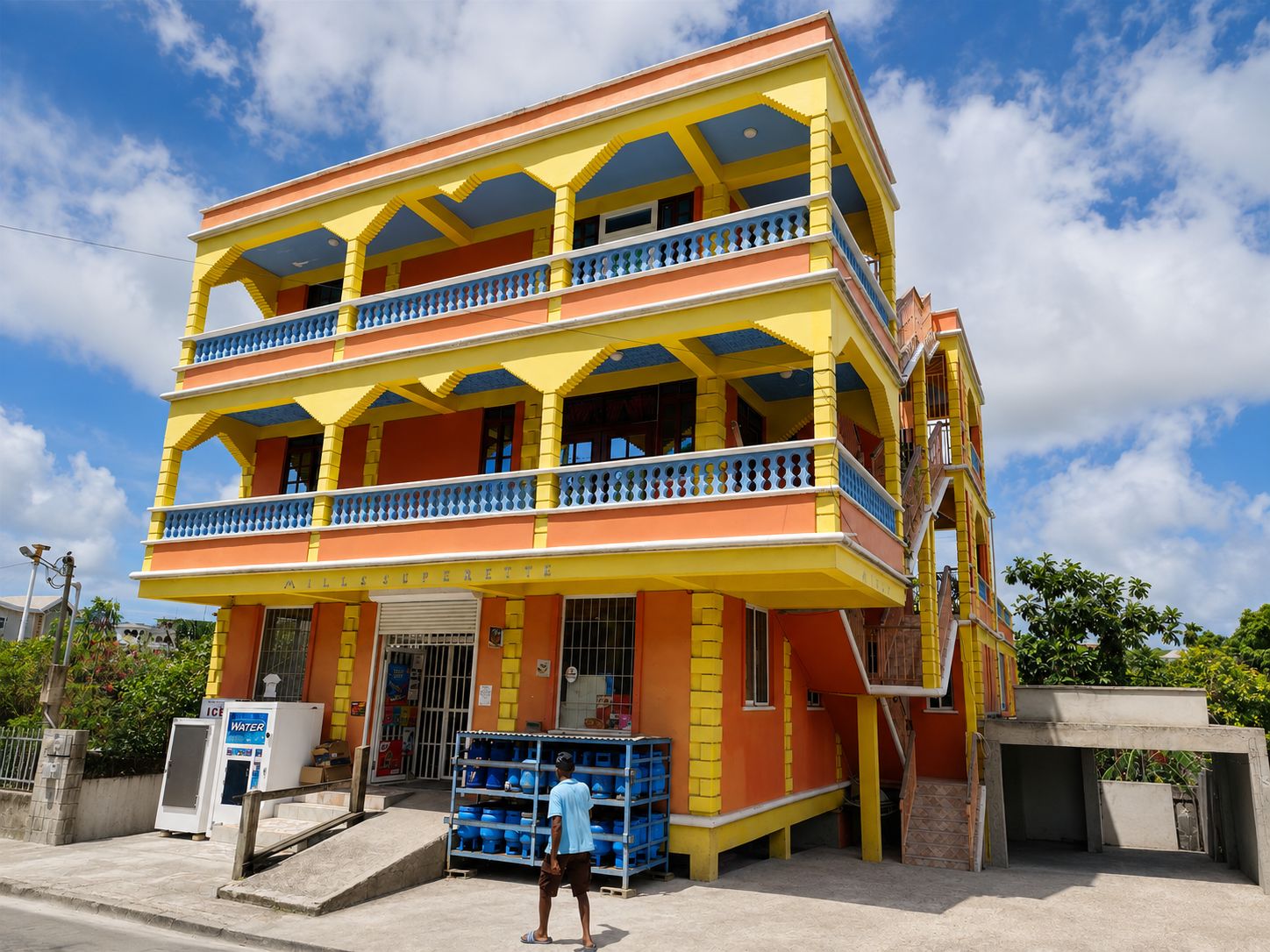 Ein mehrstöckiges Gebäude mit einer Fassade in Gelb und Orange, ein Wasserspender vor der Tür und eine Treppe zum Eingang.