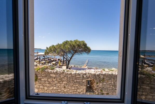 A stone wall with a tree in front of a body of water, with a clear sky above.