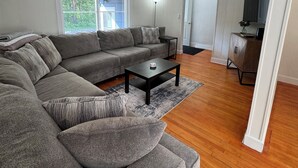 A modern living room with a sectional sofa, a coffee table, and a television in a corner. - Charming 3-bedroom 2-bathroom house with ATV access (Calumet)