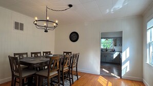 A dining area with a wooden table and chairs, a chandelier, and a clock on the wall. - Charming 3-bedroom 2-bathroom house with ATV access (Calumet)