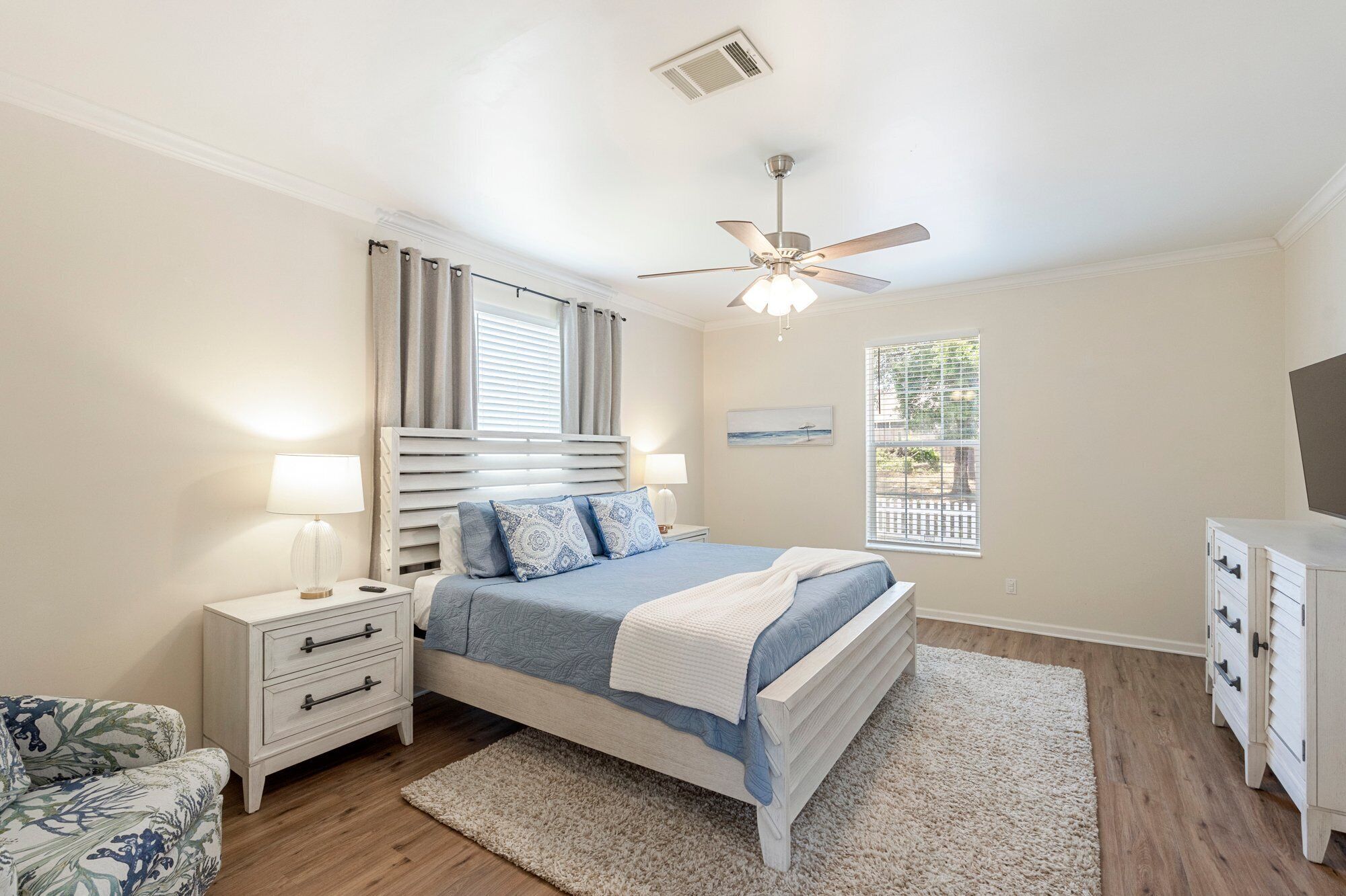 Une chambre à coucher comprenant un lit, des tables de chevet, un ventilateur de plafond, une fenêtre avec des stores et une vue sur l’extérieur.