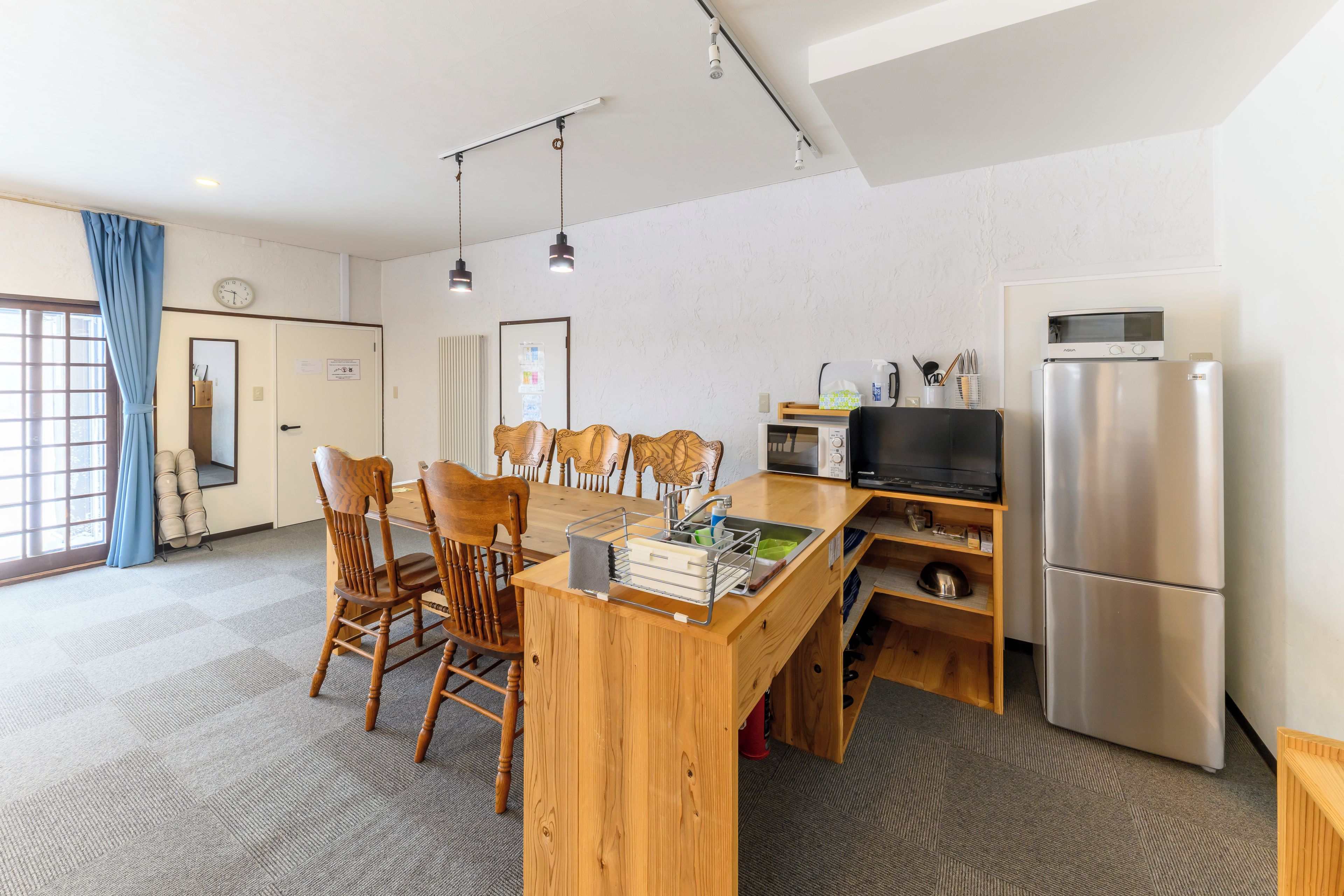 A compact kitchen with a wooden dining table, chairs, a microwave, a refrigerator, and a television.