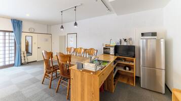 A compact kitchen with a wooden dining table, chairs, a microwave, a refrigerator, and a television.