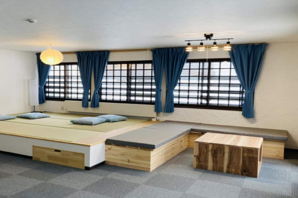 A room with a large bed, a bench, a wooden table, and a hanging light fixture.