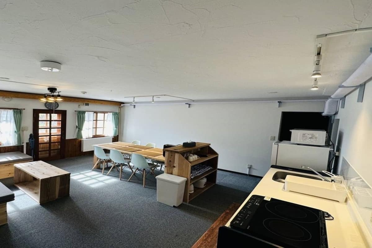 A spacious room with a large dining table, a kitchen area with a stove, and a seating area with a bench and chairs.