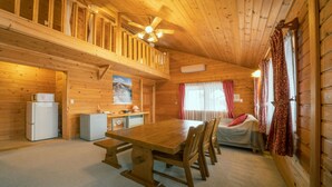 A wooden cabin with a dining area, kitchen, and a bed with curtains. - Madarao Vacances Village (Myoko)