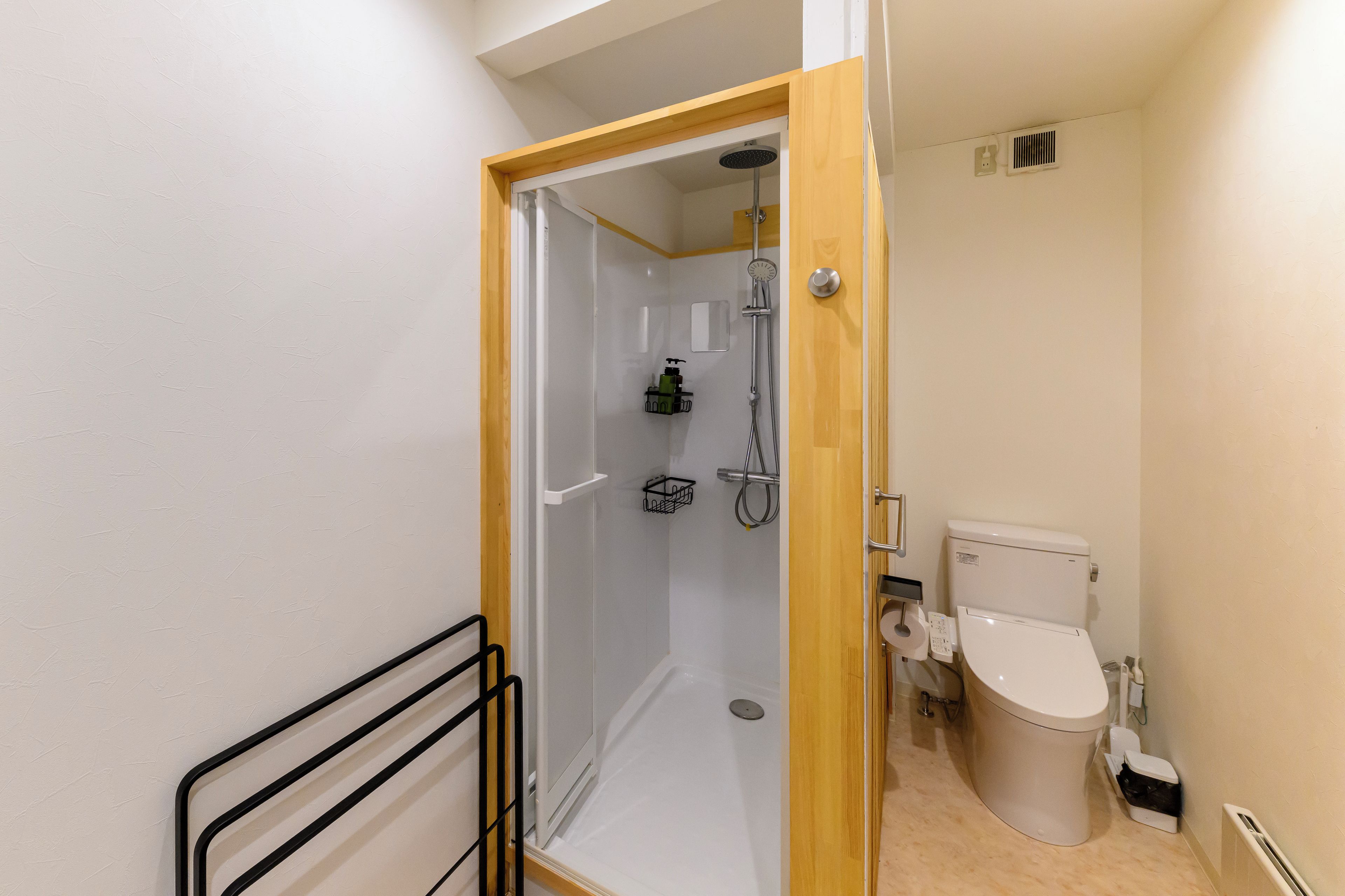 Une salle de bain avec douche, toilettes et une petite étagère où sont rangés les articles de toilette.