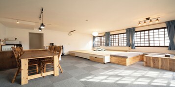 A compact living space with a dining table, chairs, a sofa bed, and a small kitchen area.