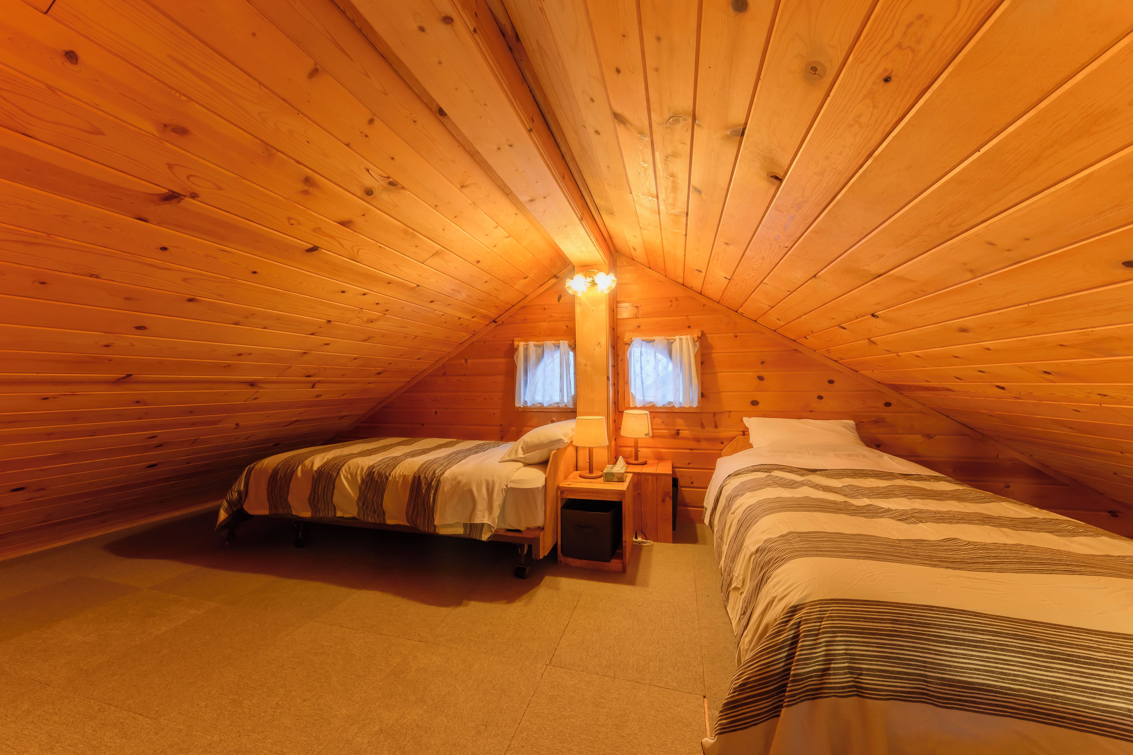 A cozy attic bedroom with two beds, a nightstand, and a lamp.