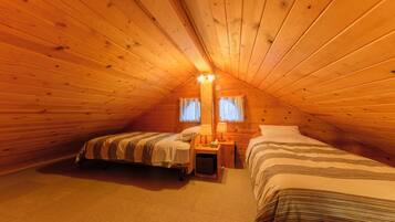 A cozy attic bedroom with two beds, a nightstand, and a lamp.