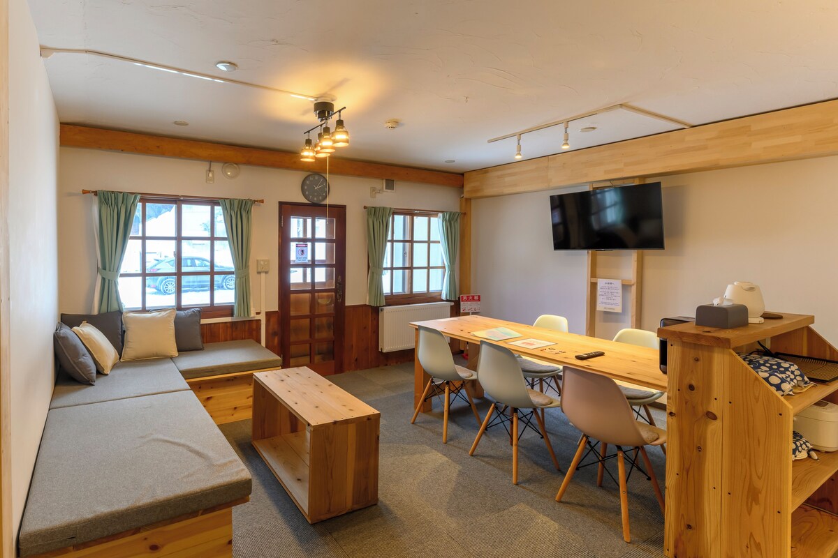 Una habitación con una mesa de comedor de madera, sillas, un sofá, un televisor y una ventana con cortinas.
