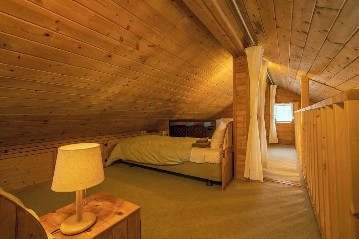 A cozy attic bedroom with a single bed, a bedside table with a lamp, and wooden walls.