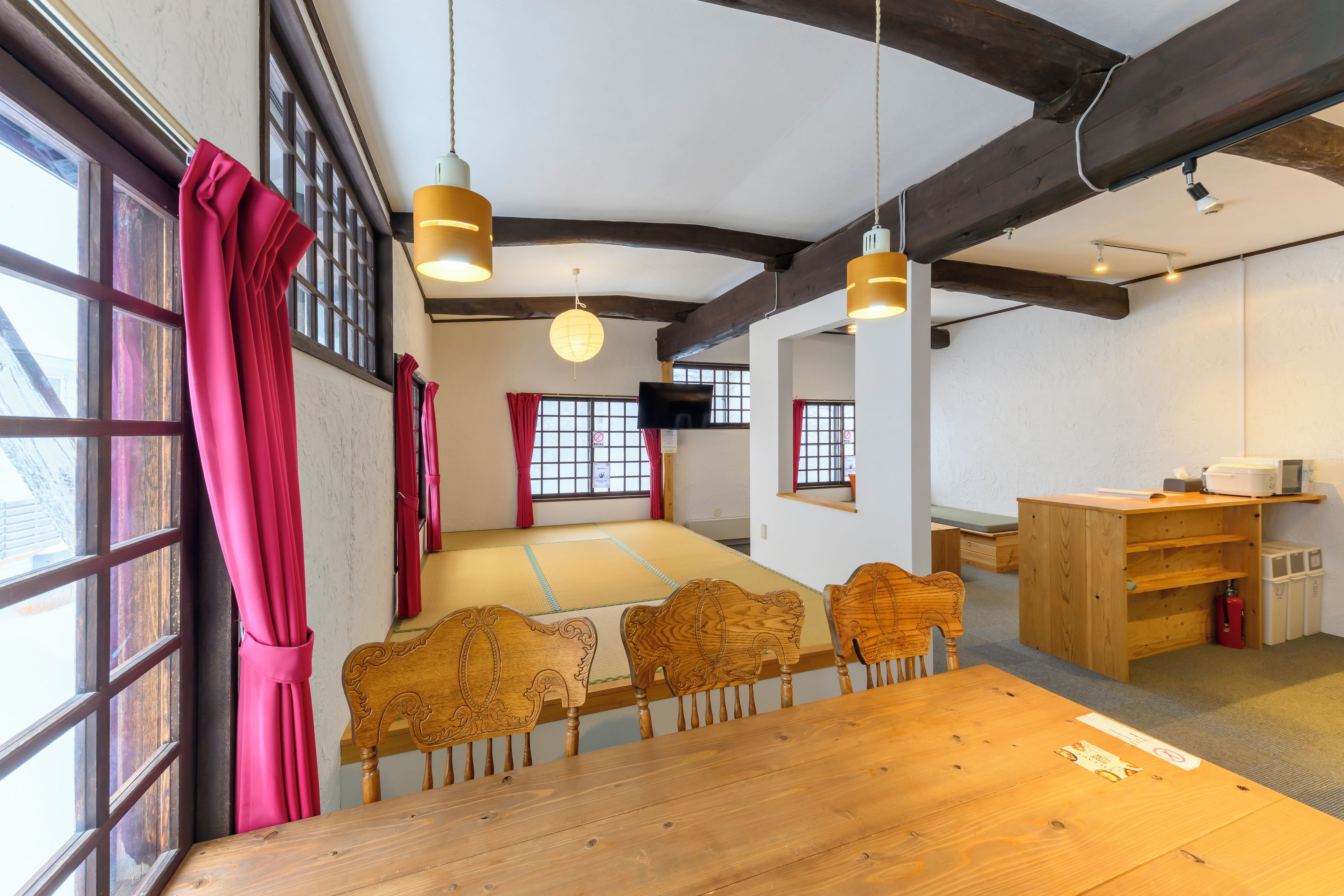 Une pièce traditionnelle avec un sol recouvert de tatamis, des meubles en bois et une grande fenêtre ornée de rideaux rouges.