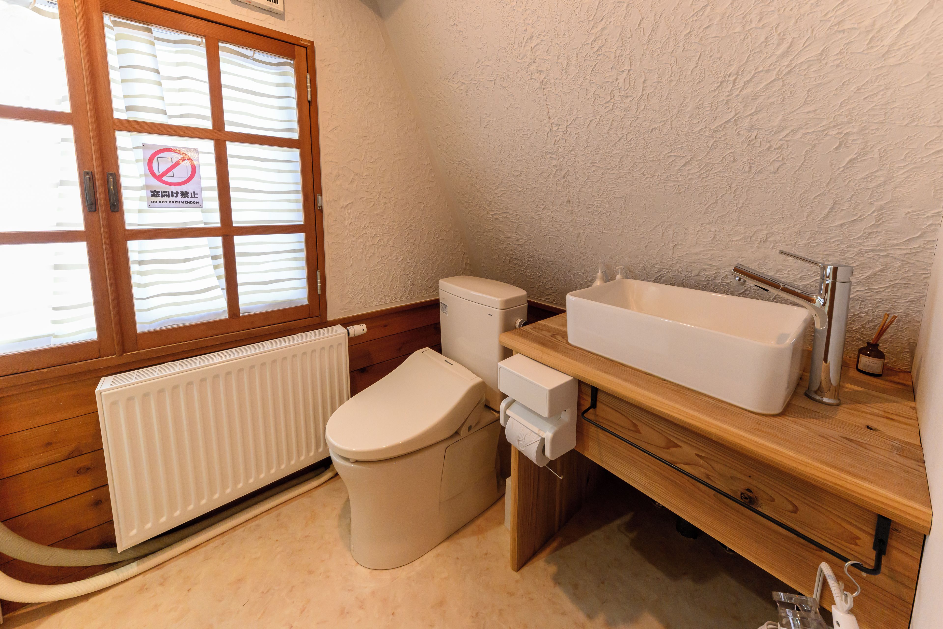 A small bathroom with a toilet, a sink, and a window with a 'Do Not Open' sign.