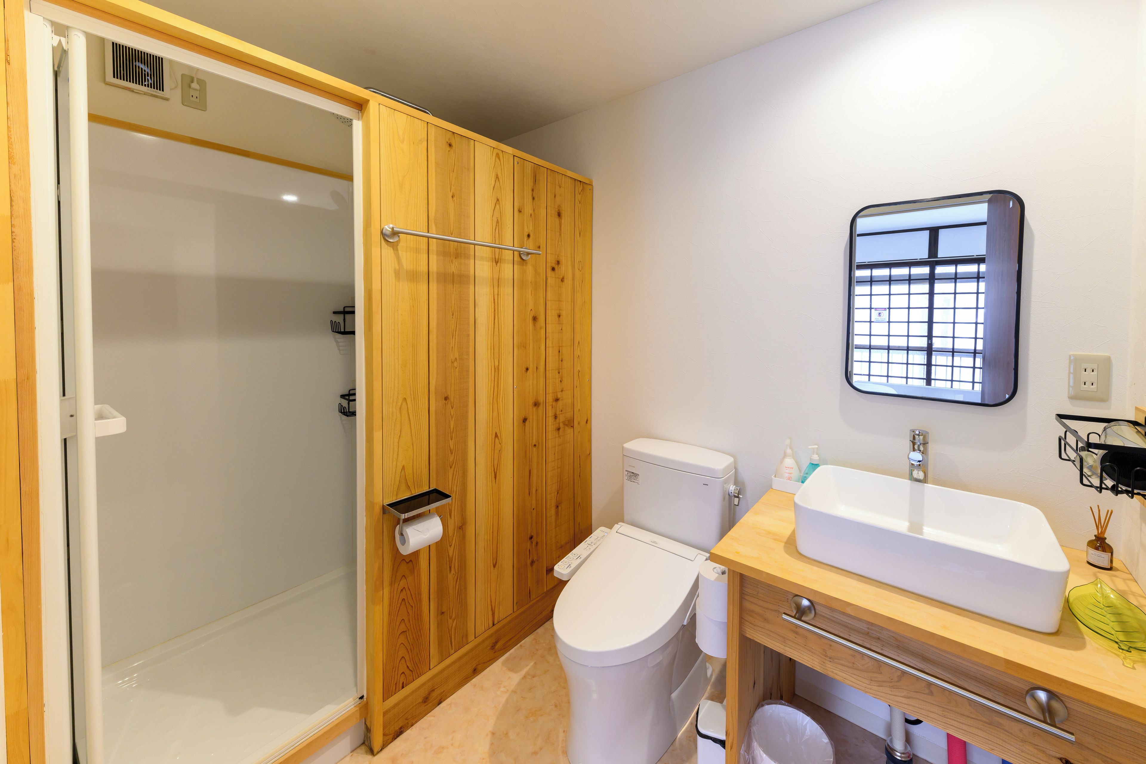 Ein Badezimmer mit Duschkabine aus Holz, Toilette, Waschbecken mit Spiegel und kleinem Fenster.
