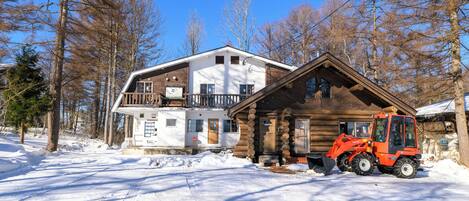 A log cabin with a snow-covered ground, a wooden exterior, and a red vehicle parked in front.