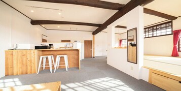 Habitación amplia con un escritorio de madera, dos taburetes blancos, un espejo grande y una ventana con cortinas rojas.