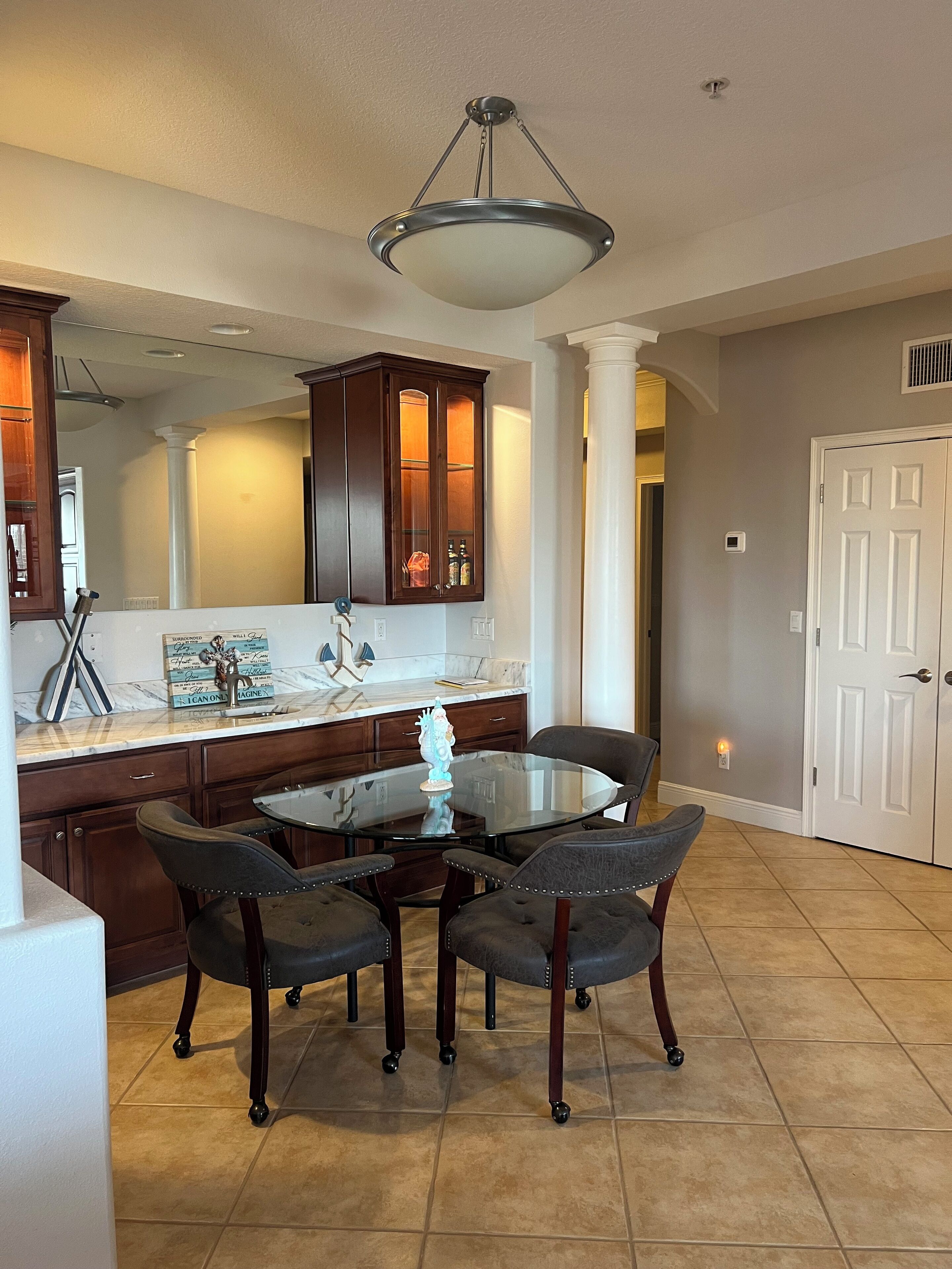 A dining area with a glass table and four chairs, a dark wooden cabinet, and a pendant light above.