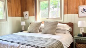 A neatly made bed with a plaid bedspread, two pillows, and a nightstand with a lamp and a book.