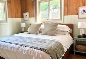 A neatly made bed with a plaid bedspread, two pillows, and a nightstand with a lamp and a book.