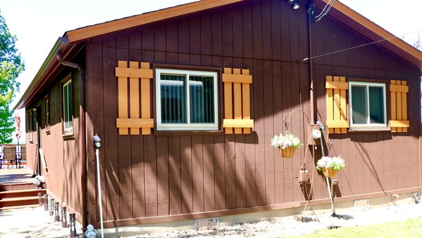 A brown building with two windows, a porch, and a small garden area with potted plants.