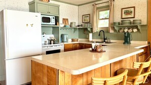 A kitchen with a central island, wooden bar stools, a refrigerator, a microwave, a stove, and a sink.