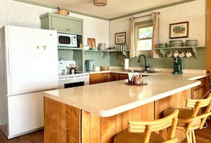A kitchen with a central island, wooden bar stools, a refrigerator, a microwave, a stove, and a sink.