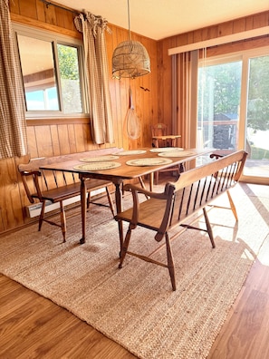 Une salle à manger en bois avec une grande table, des chaises et un tapis tissé.