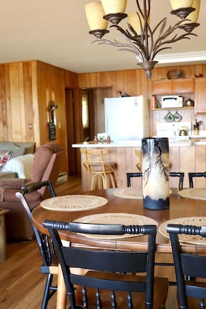 A dining area with a wooden table, chairs, and a vase centerpiece.
