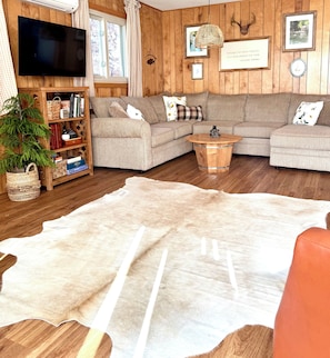 Una sala de estar acogedora con un sofá modular, un televisor de pantalla plana, paredes de madera y una alfombra grande.