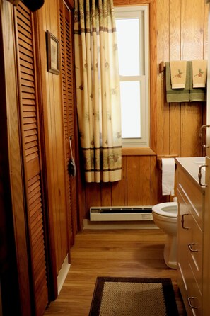 Casa de banho com painéis de madeira, com uma sanita, um porta-toalhas e uma toalha, e uma janela com cortinas.