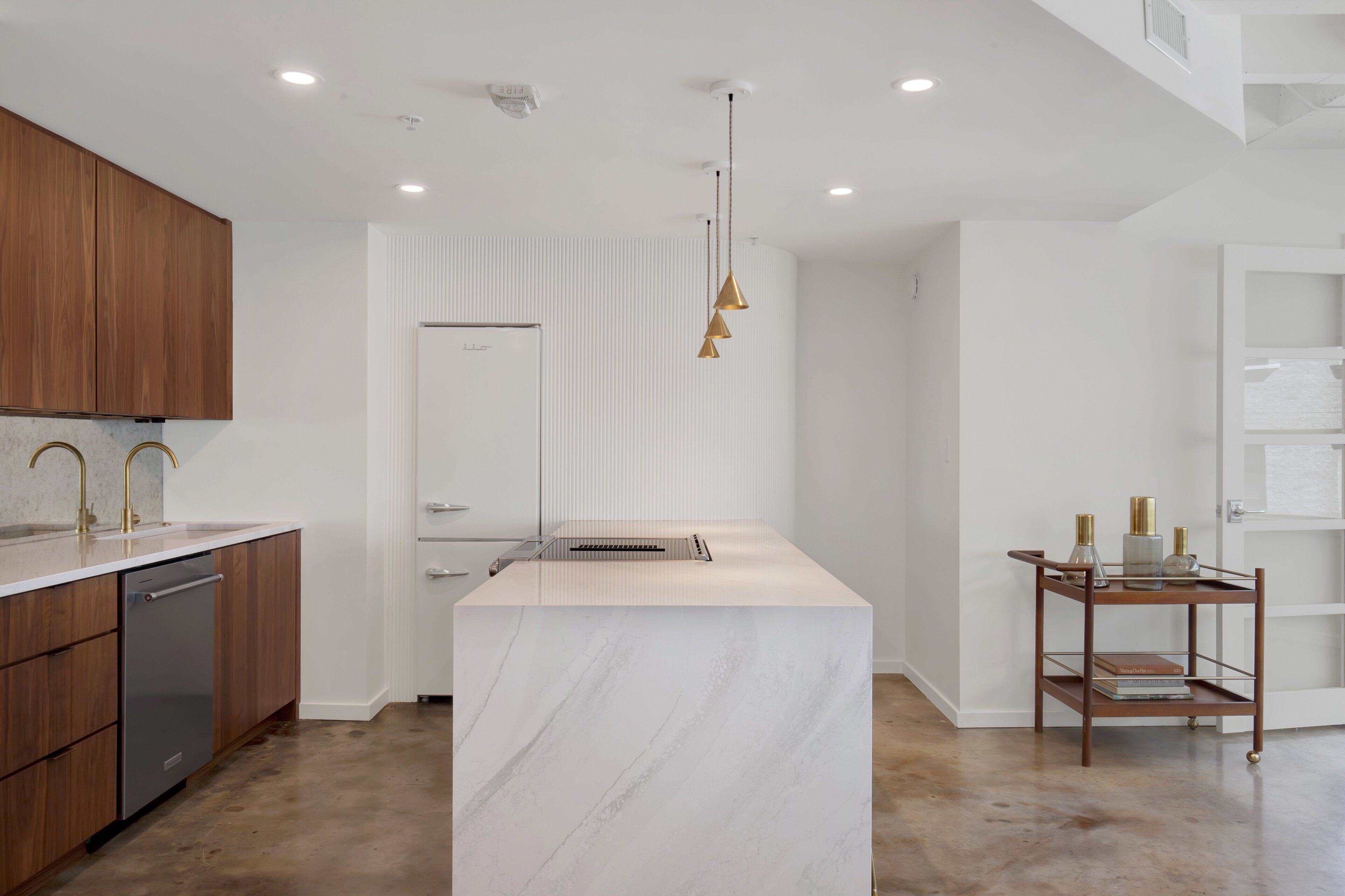 Une cuisine moderne avec un îlot en marbre, des armoires en bois et un luminaire suspendu.